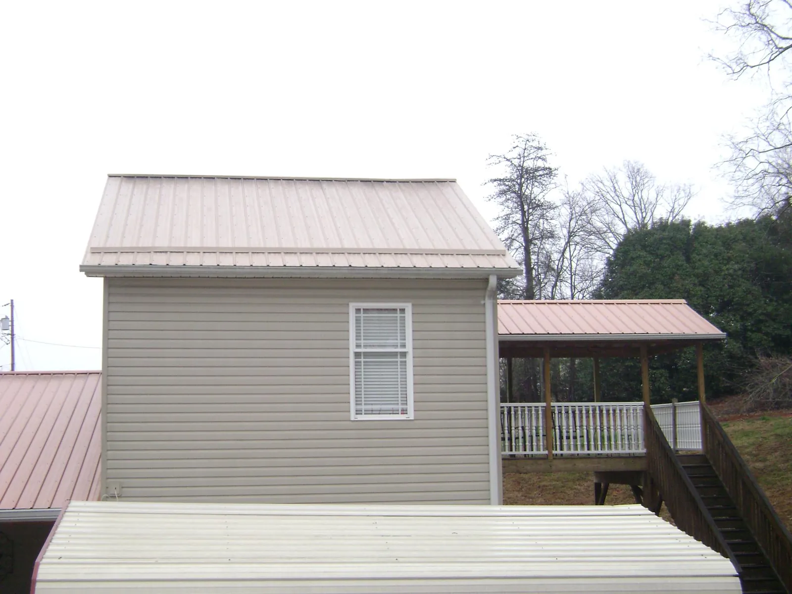 Tan metal roofs on a two story addition and attached porch, from a Roof Replacement job in Crescent